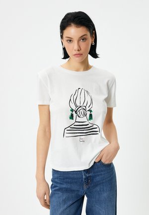 T-shirt en coton blanc avec un dessin linéaire noir du dos d'une femme avec un chignon rayé et des boucles d'oreilles vertes. Coupe décontractée, manches courtes.