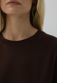 Brąsowa, krótko rękawowa koszula z okrągłym dekoltem. Gładka faktura, minimalne wykończenie przy kołnierzyku. Subtelna elastyczność materiału.