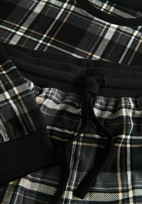 Svart och vit rutigt tyg med beige linjer har en ribbad svart midja, snöre och mudd, troligtvis en del av avslappnade byxor eller shorts.