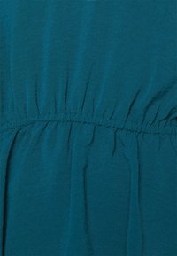 Tessuto verde acqua con una consistenza morbida, caratterizzato da dettagli arricciati in vita, creando un volume e un flusso delicati.