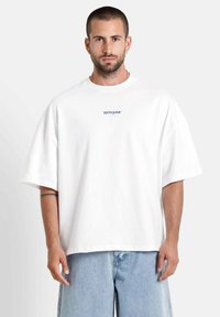 Witte oversized t-shirt van katoen, met korte mouwen en een ronde hals. Kleine blauwe tekst "SIXTH JUNE" op de borst.