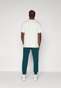 Hvid kortærmet t-shirt med en rund halsudskæring, parret med tealfarvede joggers og hvide sneakers. Glat stof med en afslappet pasform.
