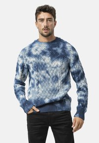 Een kabelgebreide trui in tinten blauw, met textuurovereenkomsten en geribde mouwen en zoom. Gemaakt van een zachte, gemengde stof.