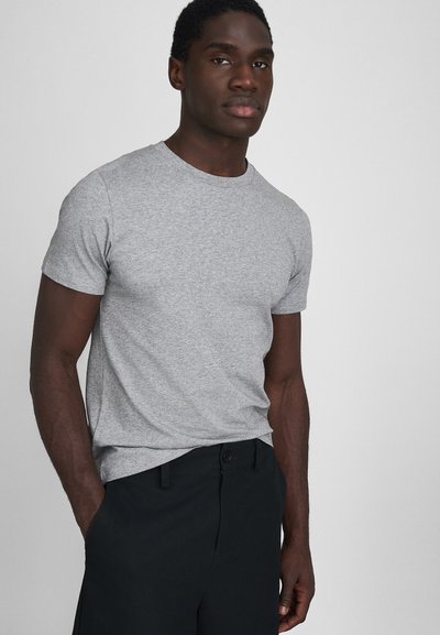Camiseta corta gris de manga corta hecha de tela suave, con un diseño clásico de cuello redondo. Combinada con pantalones negros para un look casual.