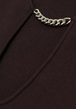 Mørkebrunt stof med en glat tekstur. Har en sølvfarvet kædeaccent ved halsudskæringen, som tilføjer et metalisk detalje til designet.