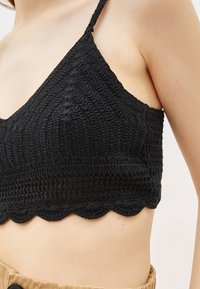 Černý háčkovaný bralet s vlnitým lemem, nastavitelnými ramínky, strukturovaným vzorem a těsným střihem. Materiál je jemný a lehký.