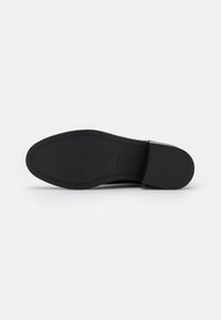Semelle de chaussure noire avec une finition lisse et mate. Présente un bout arrondi et un léger talon. Comprend des motifs de grip texturés pour l'adhérence.