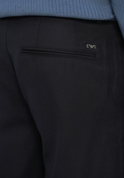 Črne krojene hlače z diskretno teksturo, ki imajo eno zadnjo žep in majhno logotipno podrobnost nad njim.