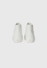 Des baskets montantes blanches avec une finition en cuir lisse, un rembourrage à la cheville et un logo discret sur le talon. Design minimaliste avec des lignes épurées.