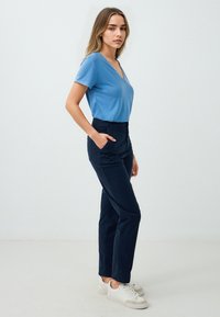 Top blu di misto cotone a maniche corte con scollo a V abbinato a pantaloni attillati blu scuro, tasche laterali e sneakers bianche; texture liscia, design casual.