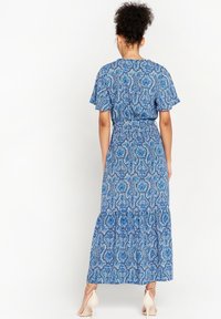 Maxi šaty s modrým paisley potiskem, vyznačující se volnými rukávy, staženým pasem a vrstvenou sukní. Vyrobeno z lehkého materiálu.