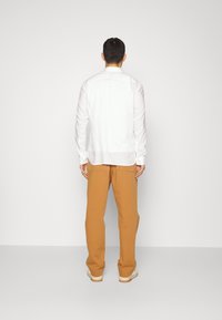 Vit långärmad skjorta med rak skärning, tillsammans med bruna vida byxor. Slätt tyg, avslappnad passform och inga synliga mönster eller detaljer.