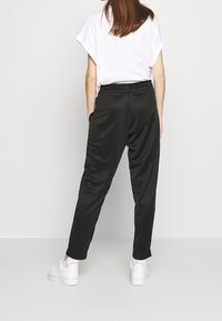 Svarta satintrousers med en avslappnad passform, elastisk midja och sidofickor. Matchas med en enkel vit t-shirt och vita sneakers.