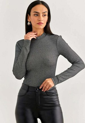 Top grigio a maniche lunghe con un collo alto, realizzato in tessuto a coste. Il modello lo abbina a pantaloni in finta pelle nera. Focalizzati sulla texture e la vestibilità.