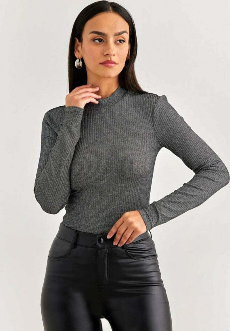 Top grigio a maniche lunghe con un collo alto, realizzato in tessuto a coste. Il modello lo abbina a pantaloni in finta pelle nera. Focalizzati sulla texture e la vestibilità.
