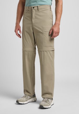 Beige cargo broek met een afneembaar ontwerp, meerdere zakken, een rechte snit en een gladde stofstructuur. Gekocht in combinatie met grijze sportschoenen.