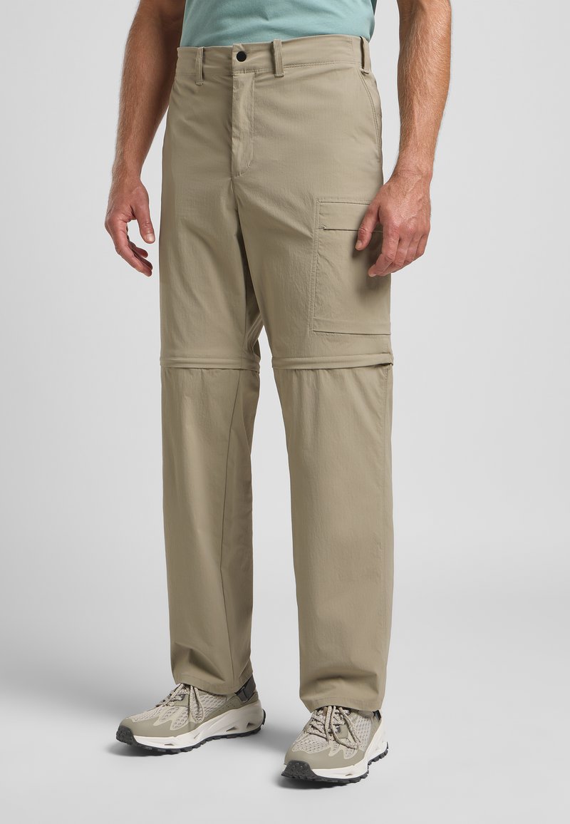 Beige Cargo-Hosen mit einem abnehmbaren Design, mehreren Taschen, geradem Schnitt und glatter Stofftextur. Getragen mit grauen Sportschuhen.