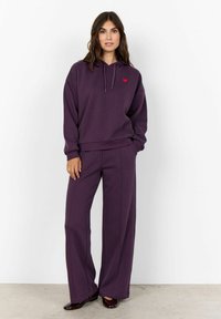 Sudadera morada y pantalones de pierna ancha a juego, hechos de una tela suave, con un pequeño logo de corazón rojo en el pecho. Textura lisa, diseño casual.