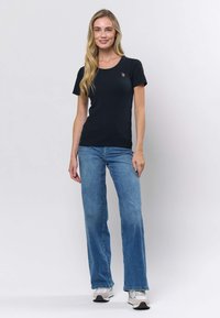 Musta ribbineulottu lyhythihainen T-paita, jossa on pyöreä pääntie ja pieni kirjailtu embleemi, yhdistettynä vaaleansinisiin liehuviin farkkuihin ja valkoisiin tennareihin.