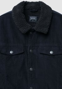 Giacca di velluto a coste blu navy con un colletto in pile nero strutturato, due tasche sul petto e bottoni a pressione argentati. L'etichetta riporta "CALLIOPE," taglia L.