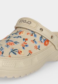 Μπεζ clog Crocs με πολύχρωμο υφασμάτινο πάνω μέρος με floral μοτίβο και ρυθμιζόμενο λουράκι στη φτέρνα με το λογότυπο Crocs.