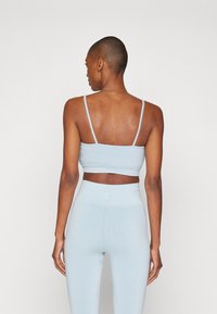 Sujetador deportivo de rayas azul claro con tirantes finos y leggings de cintura alta a juego, que muestran una textura suave y un diseño ajustado.