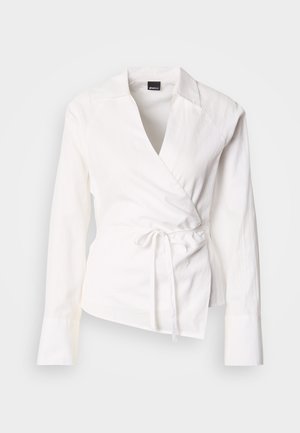 Balta ietinama krekls ar garām piedurknēm, izgatavots no viegla auduma, ar dziļu V veida kakla izgriezumu, jostu viduklim un gludu tekstūru.