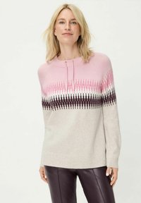Hellrosa Pullover mit einem Farbverlauf von dunkelrosa zu schwarzen Zickzackmustern. Weiche Textur, Rundhalsausschnitt und gerippte Bündchen. Kombiniert mit dunkler Hose.