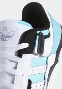 Sneaker bianca e turchese con pelle liscia e testurizzata, dettagli neri, colletto imbottito e lacci bianchi con logo sulla linguetta.