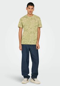 Camiseta verde claro con estampado floral, cuello redondo, mangas cortas, combinada con pantalones vaqueros de pierna ancha azul oscuro y zapatillas blancas.