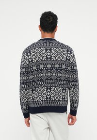 Granatowy sweter robiony na drutach z białymi geometrycznymi wzorami, ściągaczami przy mankietach i okrągłym dekoltem. Miła w dotyku faktura o klasycznym kroju.