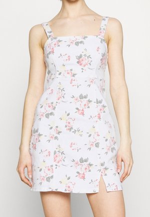 Vestido mini blanco sin mangas con patrón floral en rosa y gris y una pequeña abertura frontal en el lado izquierdo, llevado por una persona.