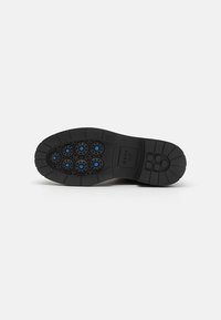 Semelle de chaussure en caoutchouc noir avec sept perforations circulaires aux accents bleus, semelle texturée et design de bord lisse.