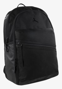 Schwarzer Rucksack aus Stoff mit glatter Oberfläche. Besitzt eine runde Form, eine vordere Reißverschlusstasche und ein schwarzes Logo an der oberen Vorderseite.