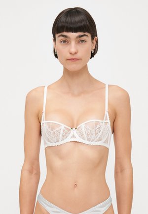 White lace bra with sheer panels, underwire support, and scalloped edges. Features a small decorative bow at the center. Adjustable straps.