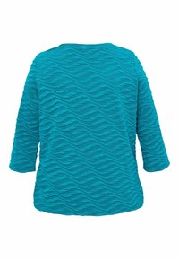 Turkizna majica s tri četvrtine rukava koja ima teksturiran, valovit vzorec po celotni površini. Gladko blago z zaobljenim izrezom.