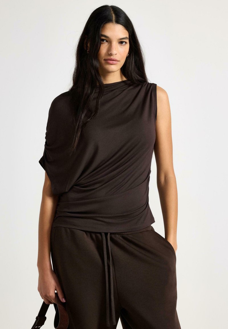 Brun, kortærmet top lavet af blødt stof, med et draperet design, asymmetrisk skulder og glat tekstur. Kombineret med matchende bukser.