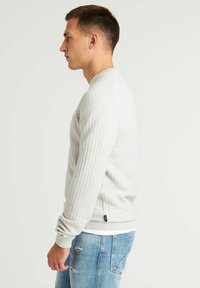 Hellgrauer Pullover mit einem strukturierten, gewebten Muster, Rundhalsausschnitt und gerippten Bündchen. Kombiniert mit hellblauen, ausgewaschenen Jeans.