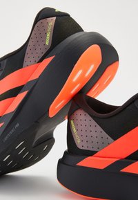 Black and gray athletic shoes featuring bright orange stripes, perforated panels, and textured material with a lightweight sole.