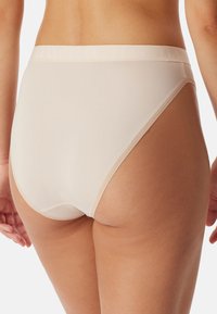 Beige korkeavyötäröiset alusvaatteet, jotka on valmistettu sileästä kankaasta. Niissä on leveä elastinen vyötärönauha, jossa on hillitty brändäys, sekä saumattomat reunat mukavuutta varten.