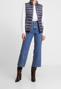 Vadderad, ärmlös väst i mörkgrått med mjuk textur; kombinerad med högmidjade, vida blå jeans och bruna klackstövlar med ormskinnsprint.