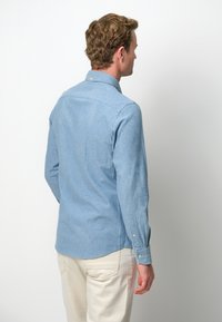 Camicia azzurra a maniche lunghe realizzata in un tessuto con una texture morbida, caratterizzata da un rinforzo sul retro, polsini con bottoni e orlo curvo.