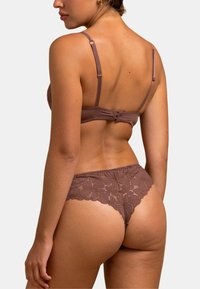 Cet ensemble de lingerie en dentelle marron présente un motif floral, des bretelles ajustables et un fermoir au dos du soutien-gorge, accompagné d'un string en dentelle assorti.