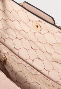 Lichtroze handtas interieur met een gladde textuur; heeft een ritszak en een herhalend "ALDO" logo patroon in een donkere tint.