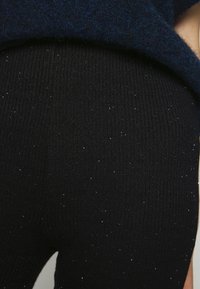 Zwarte geribbelde leggings van rekbaar materiaal, met een subtiele glitters patroon overal. Gelaagd en aansluitend ontwerp.