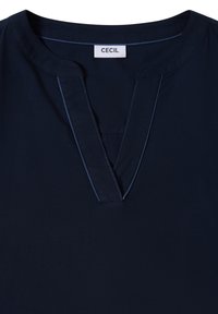 Blouse bleu marine avec un col rond et une fente en forme de V, présentant une bordure discrète cousue et une étiquette blanche portant l'inscription "CECIL" à l'intérieur du col.