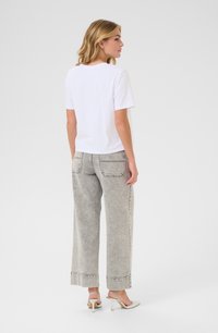 T-shirt blanche à manches courtes associé à un jean large gris clair avec une texture délavée et des poches cousues, complété par des talons clairs.