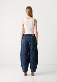 Laiad sinised denim teksad lillemustriga, kõrge vöökoht, taga taskud ja pruun nahkpatch. Kandmiseks sobiva valge triiksärgiga.