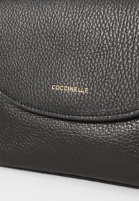 Černá kabelka z texturované kůže s přehnutým víkem. Má zlaté logo, jemné švy a hladký, odolný povrch.