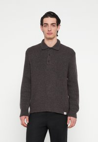 Barna kötött pulóver gallérral, három fekete gombbal és bordázott mandzsettával. Az anyag puha, texturált megjelenésű.